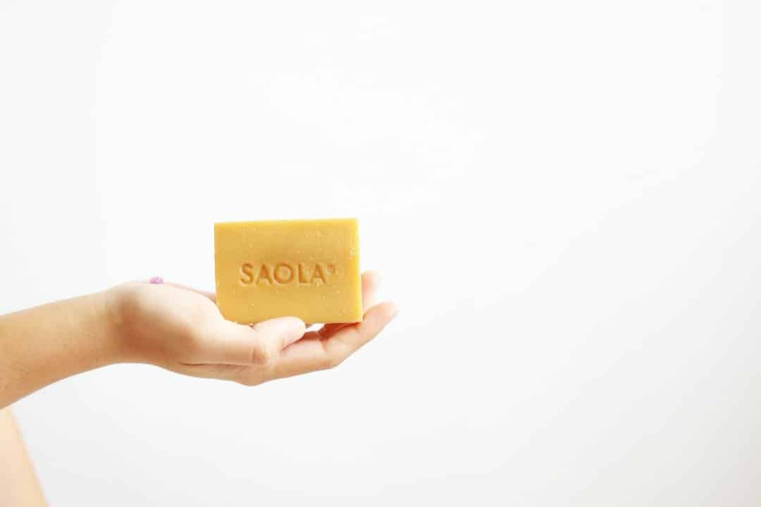 Hand holding a bar of light brown SAOLA soap.